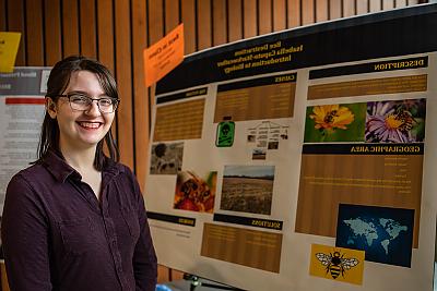 Female Student smiling and standing in front of informational poster that has 